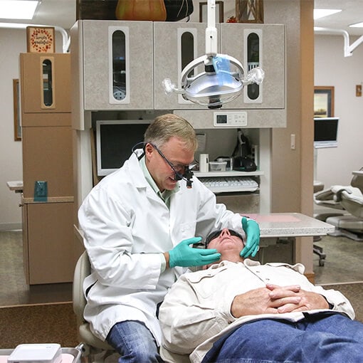 Dr. Justin Simmons checking the jaw of an elderly patient who is lying in the chair at Canyon View Dental