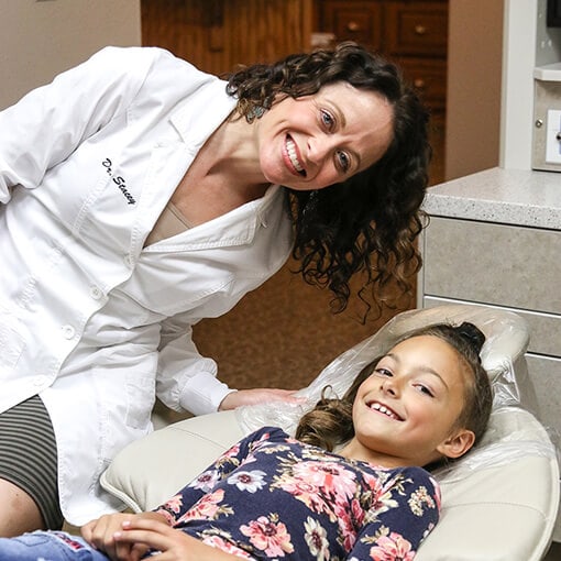 Dr. Stacey Gividen smiling while a young girl lays in the dental chair and smiles